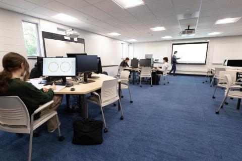 Students work at computer stations while an instructor leads a class in Westfield State University's newly renovated Center for Interdisciplinary Informatics, featuring collaborative workspaces and technology for hands-on learning.