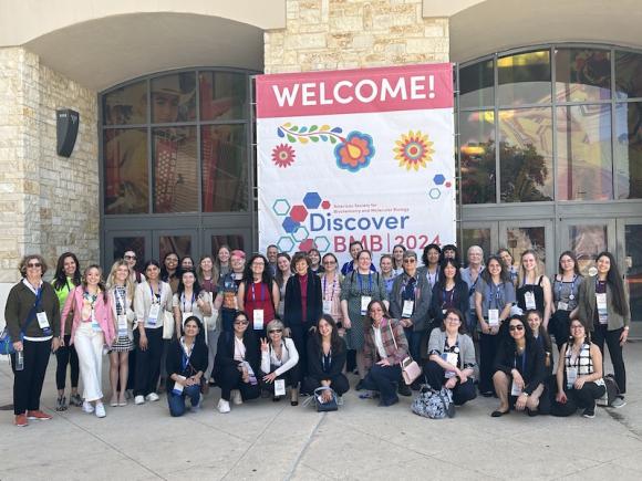 The 2024 Discover BMB Biochemistry Conference in San Antonio. A large group of people pose and smile in front a large white, pink, and blue poster which reads, "Discover BMB 2024".