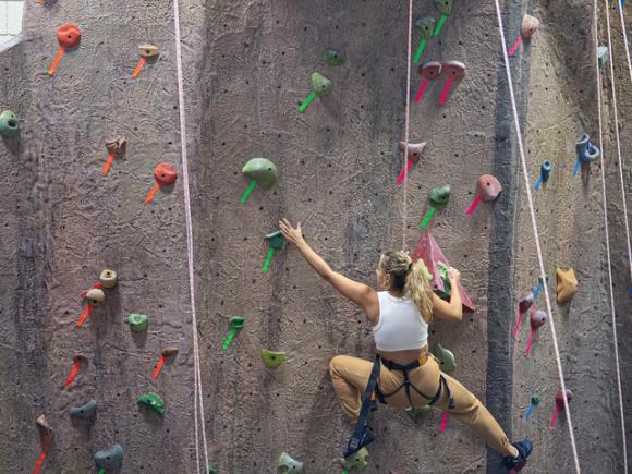 Student nearing the top of an indoor rock climbing wall.