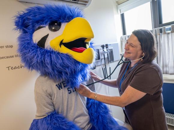 Health Services staff member checking Nestor mascot with a stethoscope.