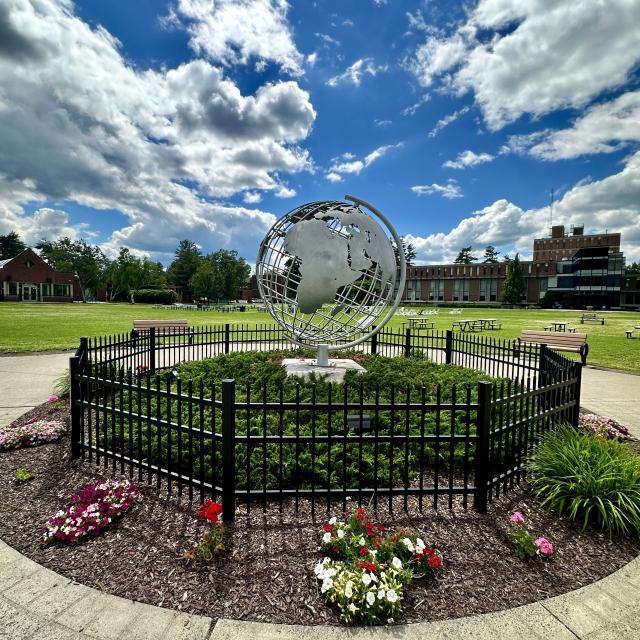 Campus globe in the summer with blue skies and colorful flowers.