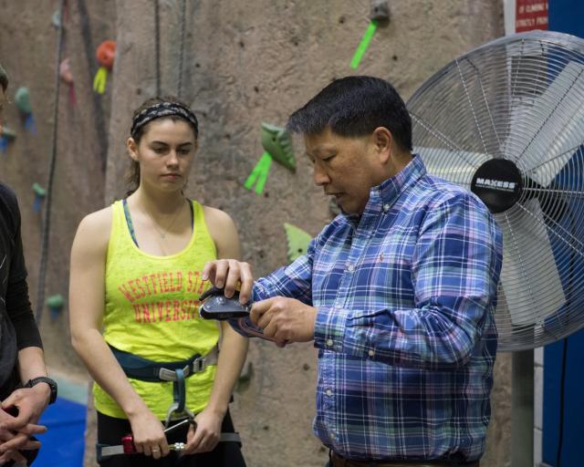 Instructor demonstrating rope-tying techniques to a student at the rock climbing wall.