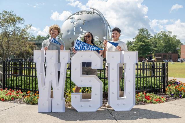 Three students standing in front of the campus globe with a large WSU sign.