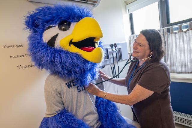 Health Services staff member checking Nestor mascot with a stethoscope.