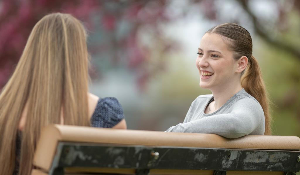 Two students sitting on a bench surrounded by pink flowering trees.